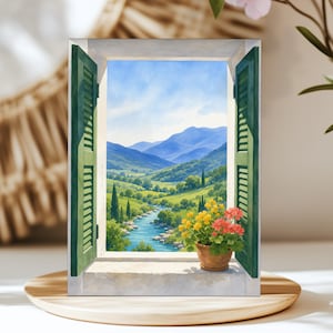 May include: A rectangular print featuring an open window with green shutters looking out onto a landscape of blue mountains, a winding river, and green hills. A terracotta pot with yellow and pink flowers sits on the white stone windowsill.