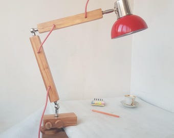 May include: A wooden desk lamp with a red metal shade and a clamp base. The lamp has a pink cord and is adjustable.