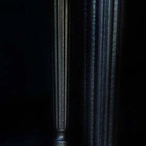 May include: Two black wooden table legs with gold-painted feet. The legs have a fluted design and are resting on a wooden floor.