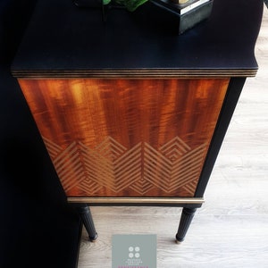 May include: A black and gold vintage cabinet with a wood grain finish and a geometric pattern on the front. The cabinet has black legs and a gold trim.
