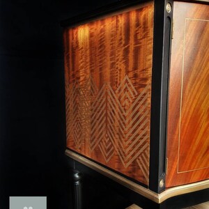 May include: A vintage wooden cabinet with black painted trim and gold accents. The cabinet has a geometric pattern on the front and sits on four black legs.