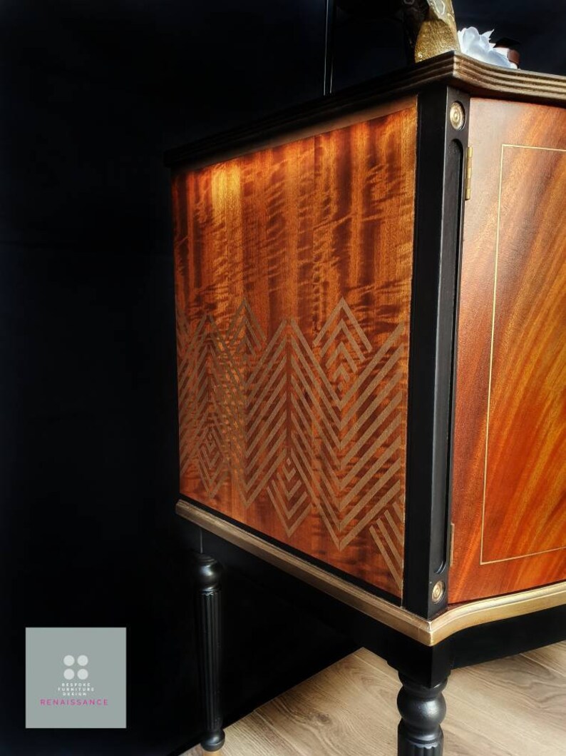 May include: A vintage wooden cabinet with black painted trim and gold accents. The cabinet has a geometric pattern on the front and sits on four black legs.