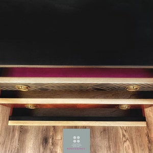 May include: A vintage wooden dresser with three drawers. The top drawer is lined with a burgundy fabric. The middle drawer has a black and gold geometric pattern. The bottom drawer is black. The dresser has gold-colored handles.