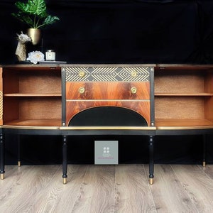 May include: A black and gold sideboard with two doors and three drawers. The doors are open, revealing shelves and a geometric pattern on the inside. The sideboard has a curved front and stands on four legs.