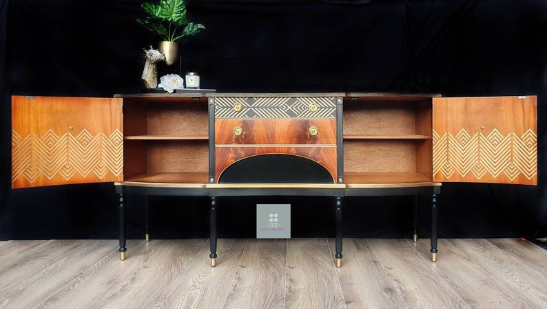 May include: A black and gold sideboard with two doors and three drawers. The doors are open, revealing shelves and a geometric pattern on the inside. The sideboard has a curved front and stands on four legs.