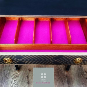 May include: A black and gold sideboard with a drawer that has a pink felt liner and wooden dividers. The drawer is open and the interior is visible. The sideboard is sitting on a wood floor.