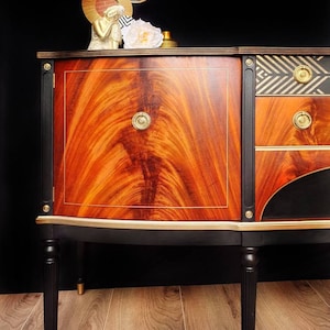 May include: A vintage wooden sideboard with black and gold painted details. The sideboard has a curved front and four legs. The top of the sideboard is decorated with a geometric pattern in black and gold.