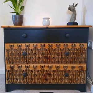 May include: A black painted chest of drawers with three drawers. The drawers have a wood veneer with a geometric pattern in black. The dresser has a modern design.