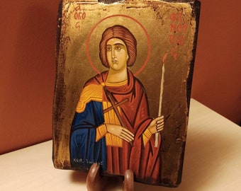 May include: A hand-painted icon of a saint holding a cross and a lit candle. The icon is on a wooden panel with a gold background and a halo around the saint's head. The text "XEIP. TWINYC" is written at the bottom of the icon.