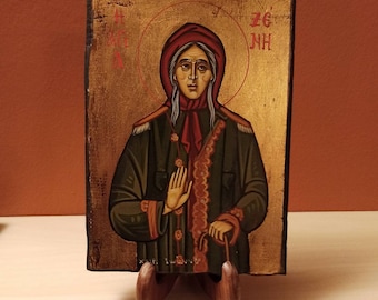 May include: Hand-painted icon of a woman with a red scarf and a gold halo. The icon is on a wooden stand and has the text "ΖΓ' ΝΗ" in red.