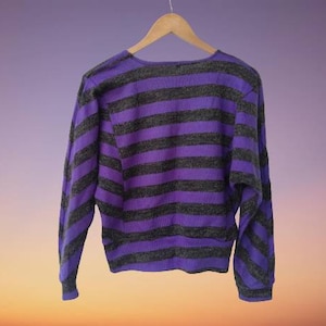 Puede incluir: Un suéter a rayas de color morado y negro con mangas largas y un corte holgado.