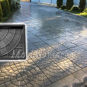 Puede incluir: Un molde de plástico negro para crear adoquines de hormigón. El molde presenta un diseño circular con un patrón radial. El molde está colocado en un patio de hormigón.