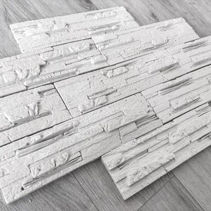 Puede incluir: Paneles de pared de piedra artificial blanca, diseñados para parecer piedra apilada. Los paneles están hechos de un material ligero y son fáciles de instalar. Son perfectos para agregar un toque rústico a cualquier habitación.
