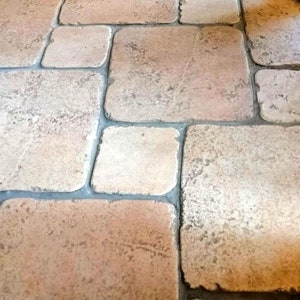 Può includere: Un primo piano di un pavimento in terracotta con un motivo di piastrelle quadrate disposte a spina di pesce.