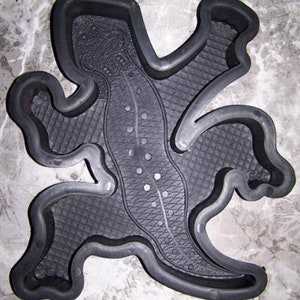May include: Black rubber mold of a lizard with a textured surface. The mold is designed for making concrete or plaster castings.