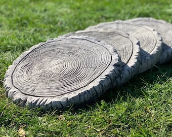 May include: Four gray concrete stepping stones shaped like tree stumps. The stones are arranged in a row, with the largest stone in the front and the smallest stone in the back.