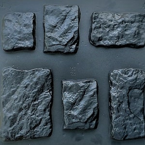May include: Six dark grey, rectangular stone moulds with textured surfaces. The moulds are arranged in two rows of three, showcasing a rough, natural stone appearance. Ideal for creating decorative garden elements.