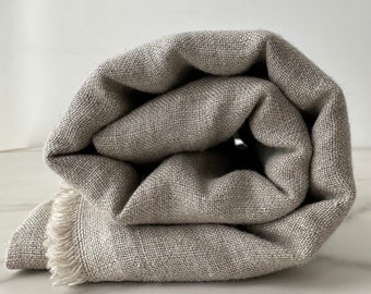 May include: A rolled up beige linen throw blanket with a fringe edge.