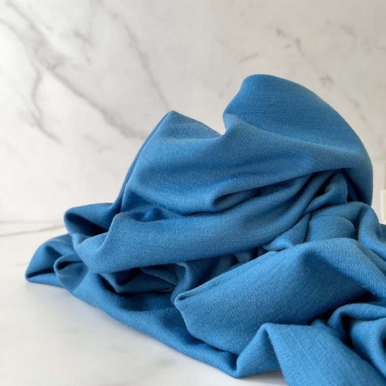 May include: A crumpled piece of soft, blue fabric. The fabric is smooth and has a slight sheen.
