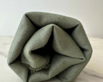 May include: A sage green linen fabric rolled up into a circular shape. The fabric has a slightly textured surface.