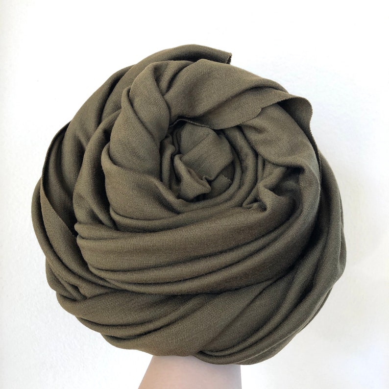 May include: A soft, olive green fabric scarf is rolled up into a rose shape.