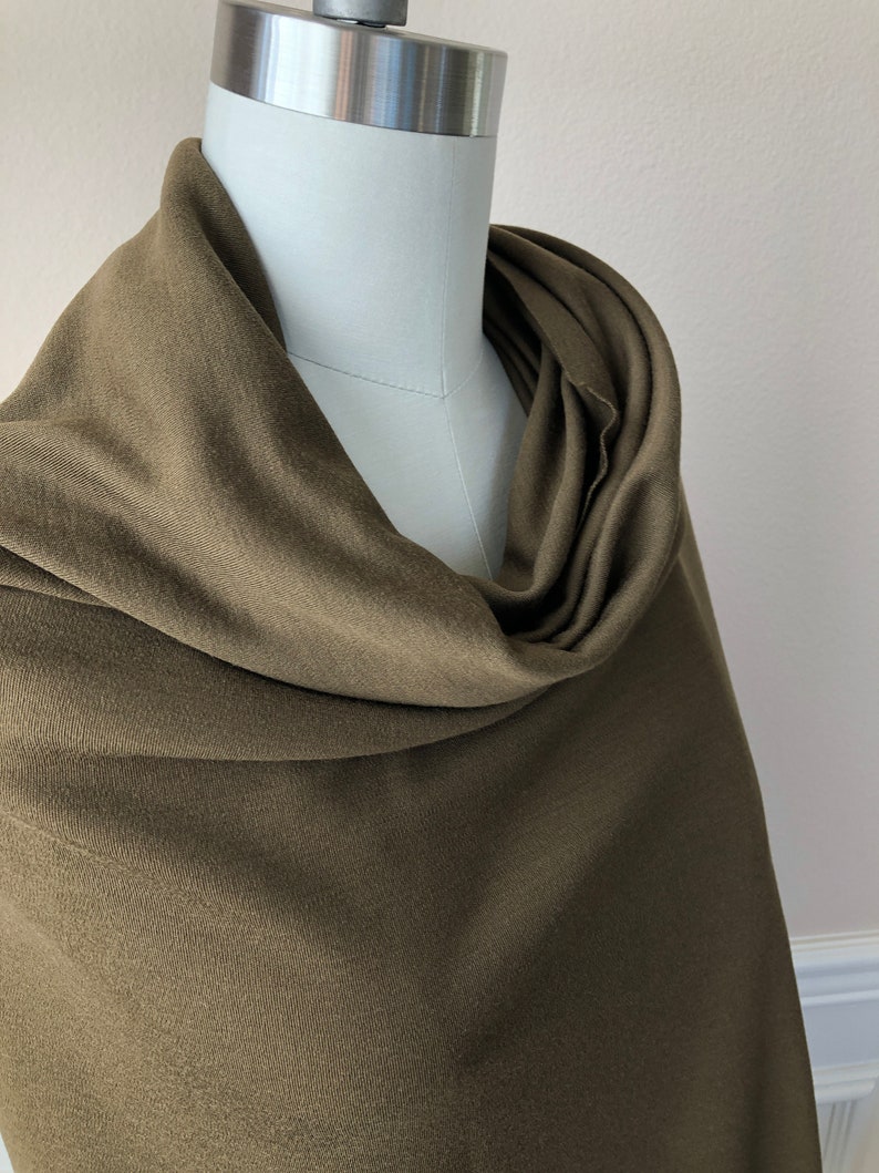 May include: A soft, olive green scarf draped over a mannequin. The scarf is made of a smooth, lightweight fabric.