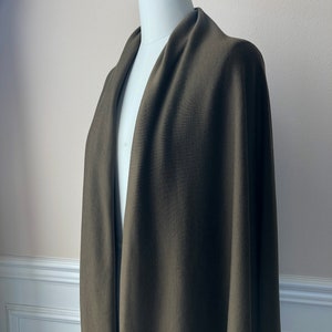 May include: A dark green, long, rectangular shawl or wrap made of a soft, knit fabric. The shawl is draped over a white mannequin.