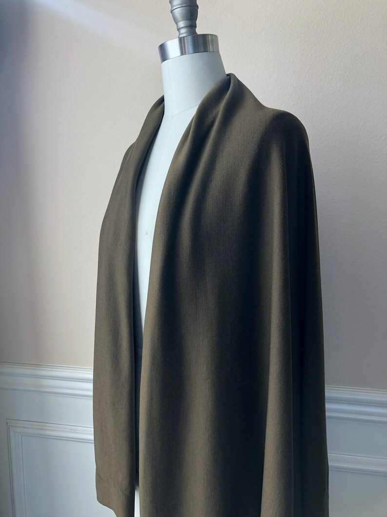 May include: A dark green, long, rectangular shawl or wrap made of a soft, knit fabric. The shawl is draped over a white mannequin.