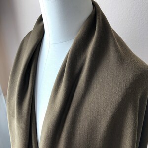 May include: A close-up of a dark green fabric draped over a white dress form. The fabric has a subtle texture and a smooth finish.