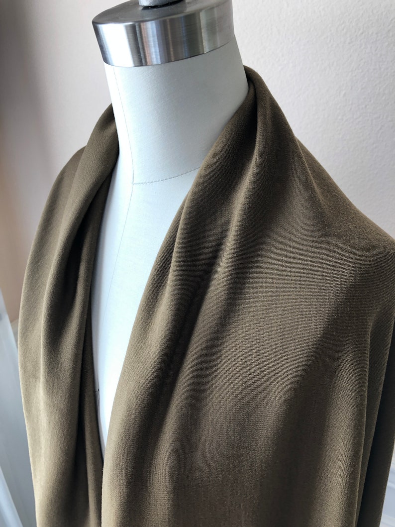 May include: A close-up of a dark green fabric draped over a white dress form. The fabric has a subtle texture and a smooth finish.