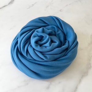May include: A soft, blue fabric scarf rolled into a circle.