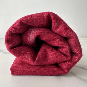 May include: A rolled up burgundy fabric with a textured weave.