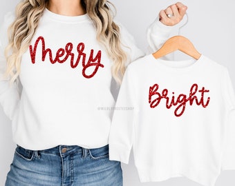 May include: White long-sleeved shirts with red glitter lettering. The larger shirt says "Merry" and the smaller shirt says "Bright".