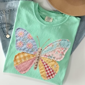 May include: A white ceramic mug with a black handle and the text "But First, Coffee" in a black, bold font. The mug is on a white surface.