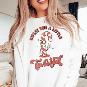 May include: White long-sleeve sweatshirt with a red and white candy cane graphic and the text "Sweet but a little Twisted".