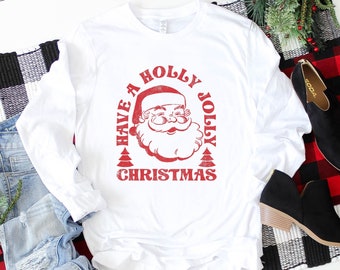 May include: White long-sleeved t-shirt with a red vintage-style graphic of Santa Claus and the text "Have a Holly Jolly Christmas".