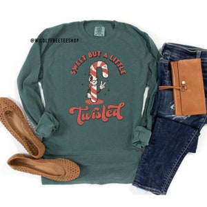 May include: A green long-sleeved t-shirt with a cartoon candy cane holding a peace sign and the text "Sweet but a little twisted".