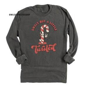 May include: A dark gray long-sleeve t-shirt with a vintage-style graphic of a candy cane with a face and the text "Sweet But A Little Twisted".