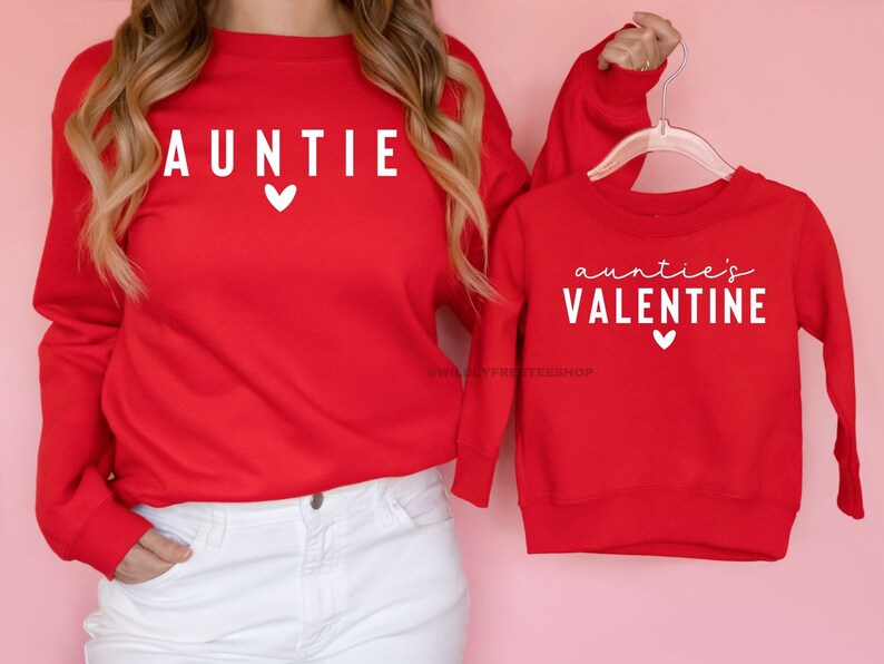 Może przedstawiać: Dwie czerwone bluzy z długimi rękawami z białym tekstem. Większa bluza ma napis "AUNTIE" z małym sercem. Mniejsza bluza ma napis "auntie's VALENTINE" z małym sercem.