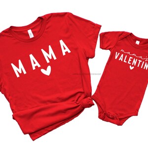May include: Red t-shirt with the word "MAMA" in white with a small white heart. A red baby onesie with the text "mama's VALENTINE" in white with a small white heart.