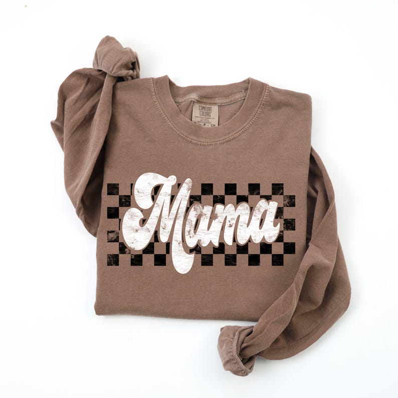 Puede incluir: Una camiseta de manga larga marr&oacute;n con la palabra "Mama" en una fuente blanca retro sobre un fondo a cuadros blanco y negro.
