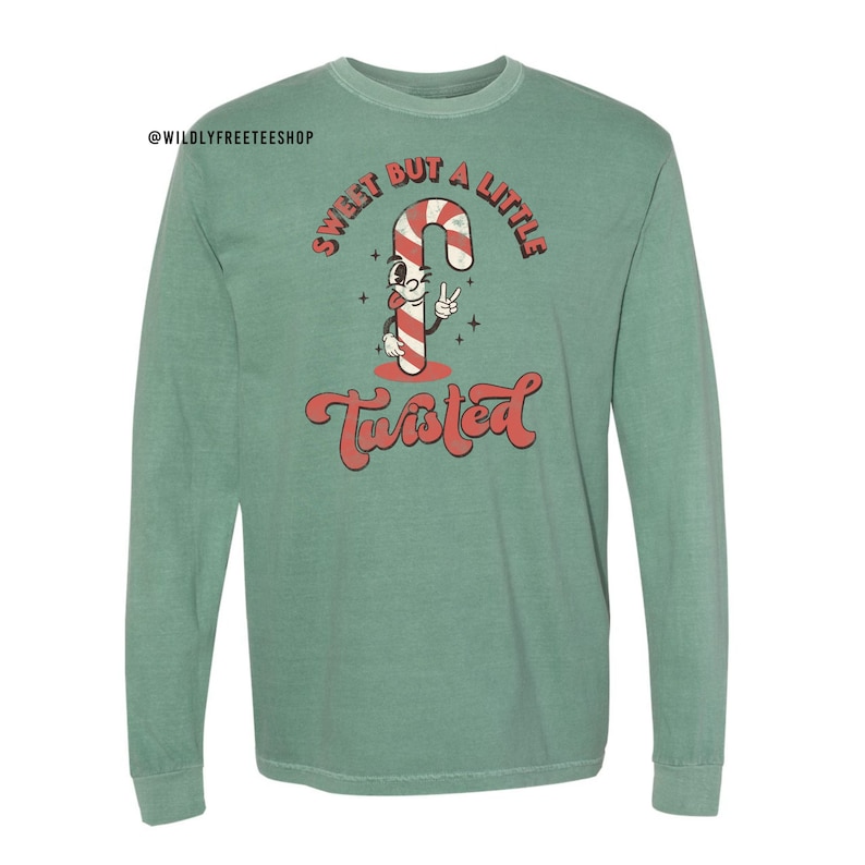 May include: A green long-sleeved t-shirt with a vintage-style graphic of a candy cane with a face and the text "Sweet but a little twisted".