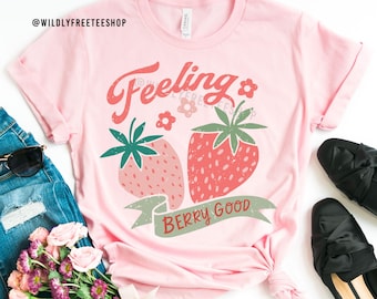 May include: Pink t-shirt with a graphic of two strawberries and the text "Feeling Berry Good".
