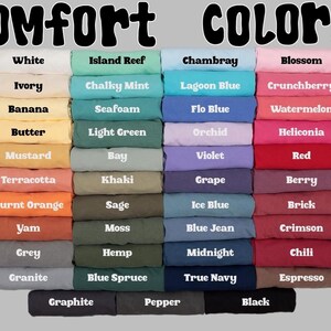 May include: Image displaying a color chart with the words "Comfort COLORS" at the top. The chart features a variety of folded fabric samples in shades like white, blue, pink, and green, each labeled with a color name.