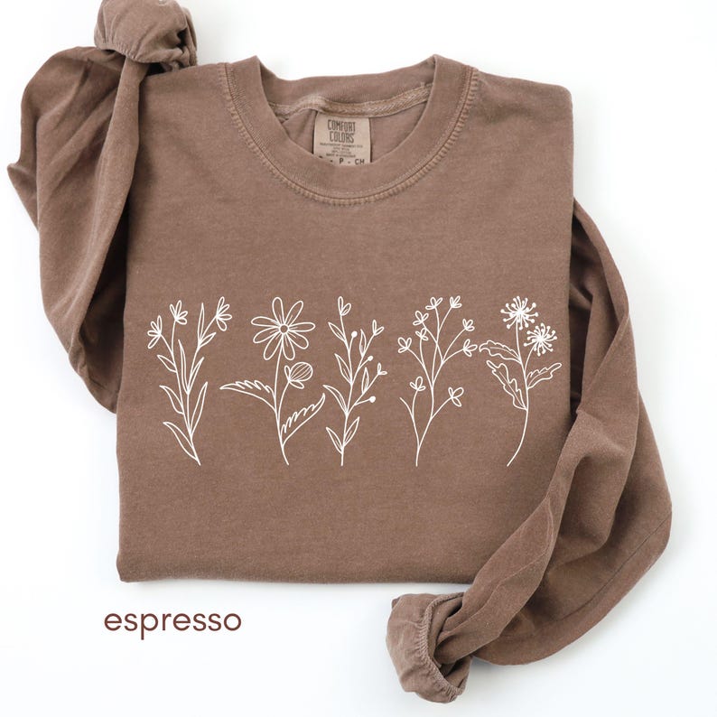 May include: Espresso-colored long-sleeve shirt with a white floral design across the front. The shirt features a crew neck and the word "espresso" at the bottom. The shirt is made of a soft material.