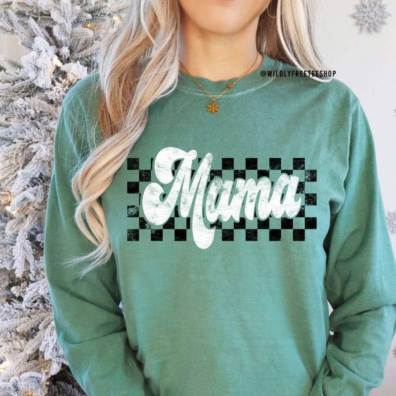 Puede incluir: Una camiseta de manga larga verde azulada con un gr&aacute;fico blanco de estilo vintage "Mama" sobre un fondo a cuadros blanco y negro.
