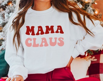 Op de afbeelding: Wit sweatshirt met de tekst "MAMA CLAUS" in rode en roze retro letters.