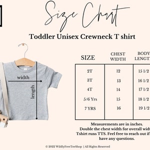 May include: A light gray toddler unisex crewneck t-shirt on a wooden hanger, with a size chart. The chart shows chest width and body length measurements in inches for sizes 2T to 7 YRS. The text on the image says "Wildly Free Tee Shop".