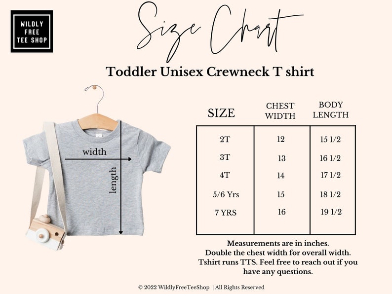 May include: A light gray toddler unisex crewneck t-shirt on a wooden hanger, with a size chart. The chart shows chest width and body length measurements in inches for sizes 2T to 7 YRS. The text on the image says "Wildly Free Tee Shop".