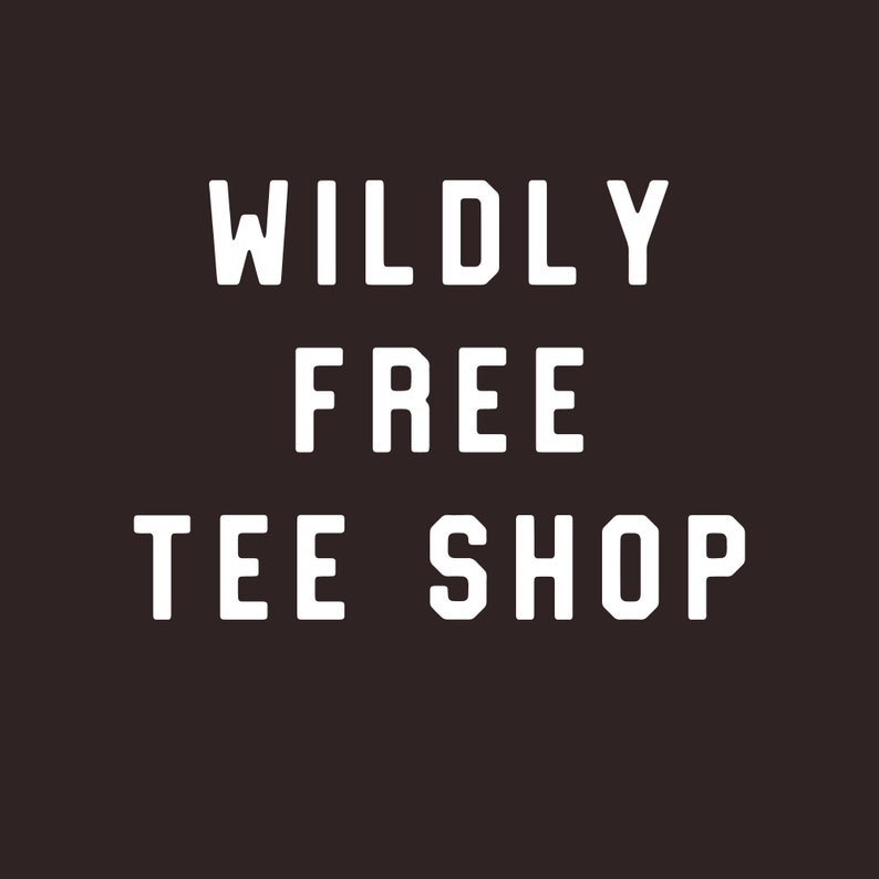 May include: White text on a dark brown background reads "WILDLY FREE TEE SHOP" in a bold, sans-serif font. The text is centered and stacked, creating a simple yet impactful design.